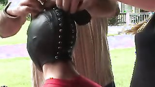 Latex-clad slave putting on her creepy mask outdoors