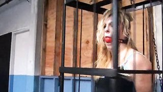 Slutty blonde in leather pants is kept in a cage